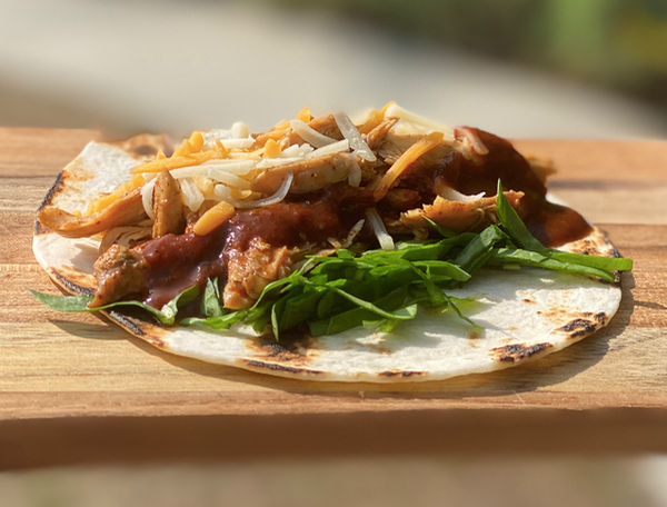 Pulled chicken taco on toasted tortilla with shredded cheese and arugula